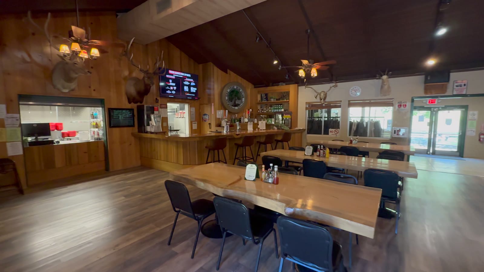 Inside the Club House Bar & Grill: the kitchen window under the trophy mounts, the bar with its stools, and the long wooden tables.