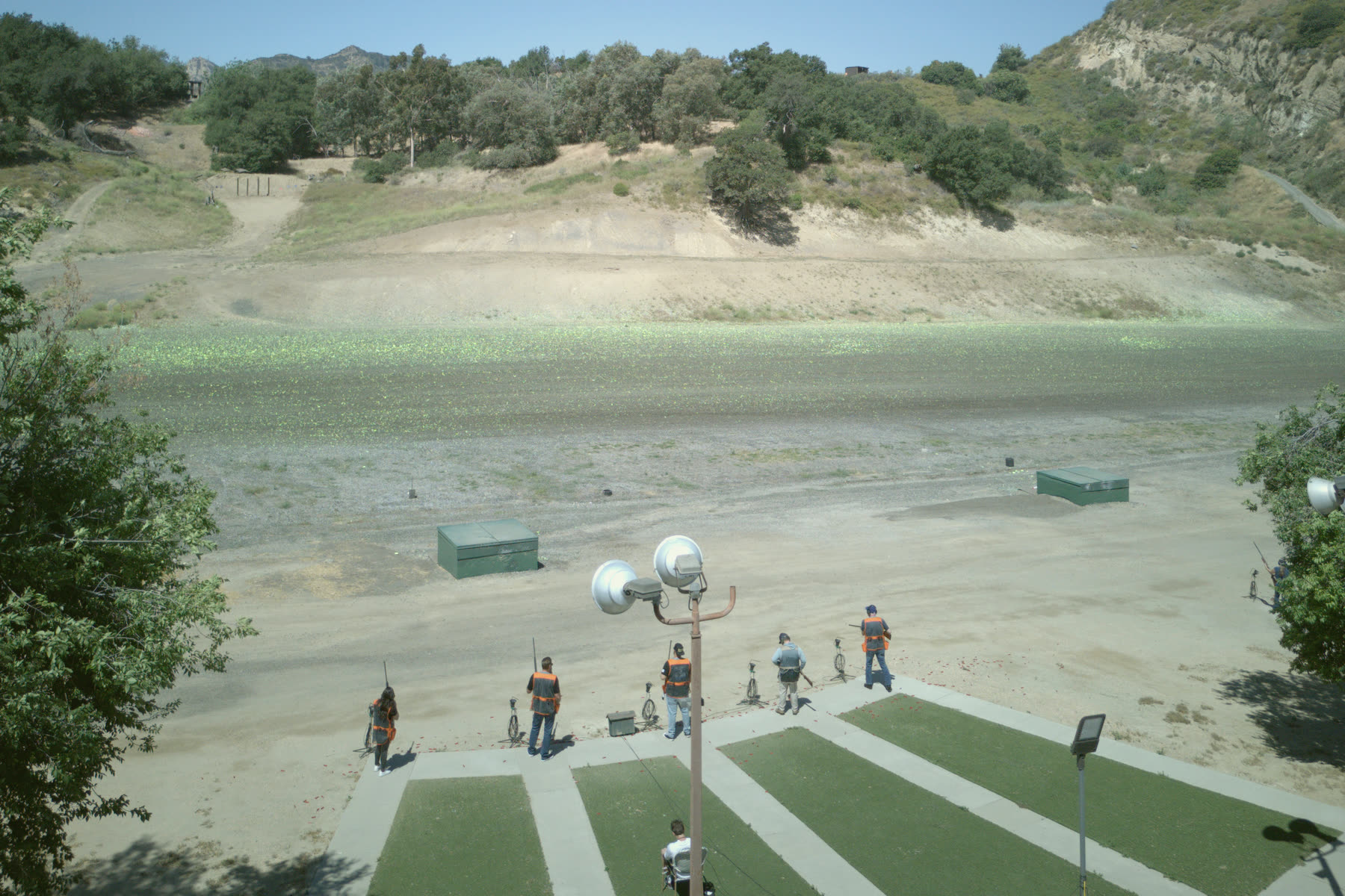 A trap field from above: a squad at the pads, the trap house on the field and the wooded hill beyond.
